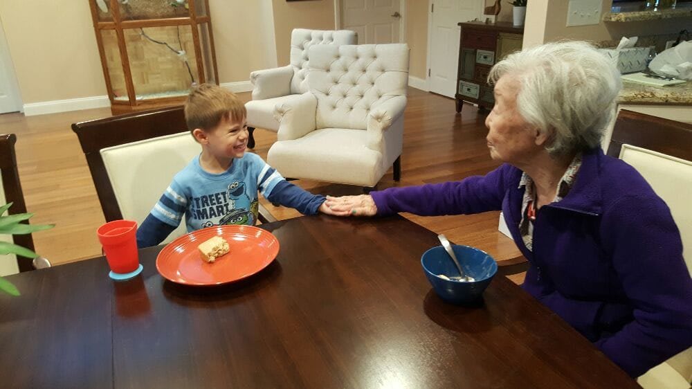 A young boy and an elderly woman share a touching moment at the dining table, holding hands while enjoying their meal.