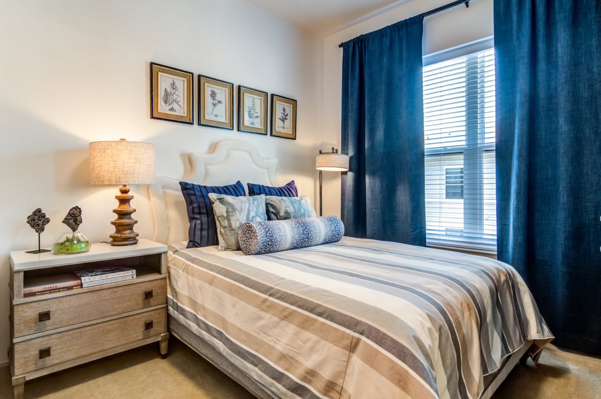 A cozy bedroom featuring striped bedding, blue curtains, and wall art.