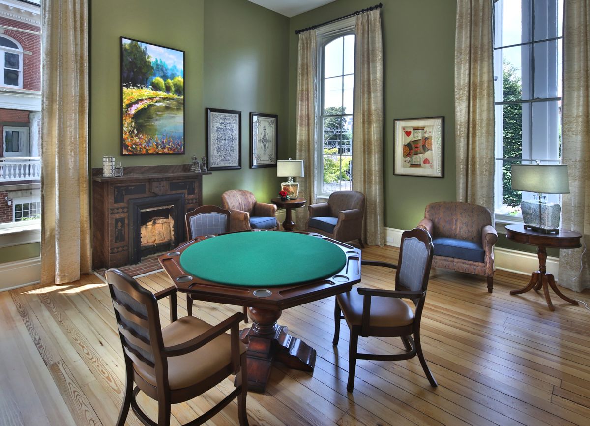 A classic room with a poker table surrounded by chairs, featuring green walls and framed artwork.