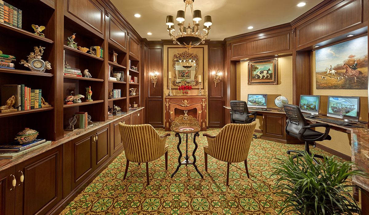 A cozy library room with elegant wood paneling, featuring bookshelves, a decorative fireplace, and comfortable seating.