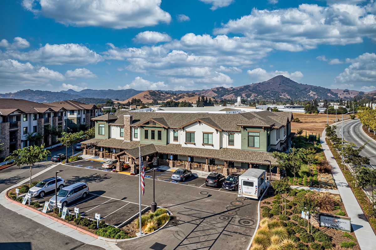 A scenic view of a building with a parking lot, set against a backdrop of mountains and a cloudy sky.