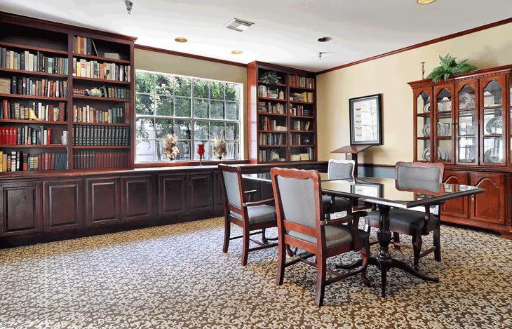 A cozy library room with bookshelves, a window, and a table with chairs.