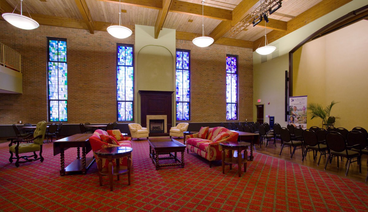 A spacious room with comfortable seating, featuring stained glass windows and a fireplace.