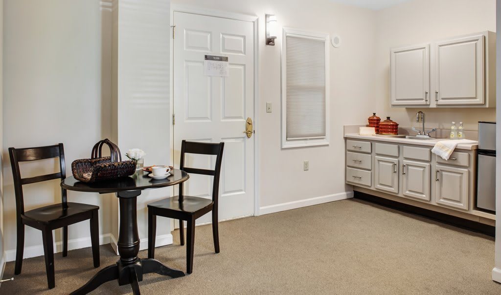 A cozy room interior featuring a small round table with a chair, adjacent to a door and bathroom vanity.