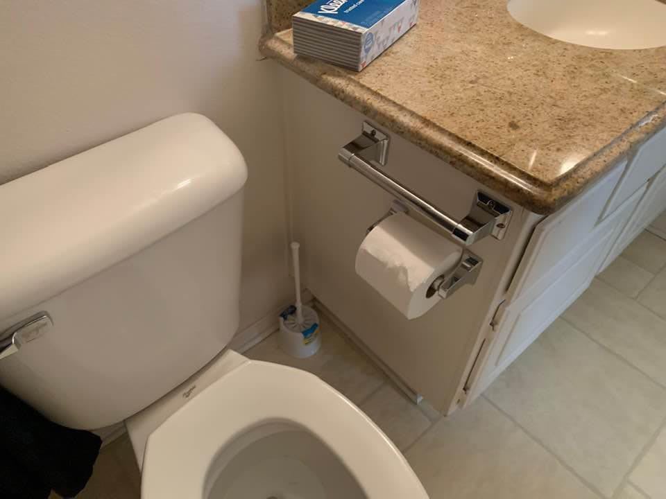 A bathroom with a toilet, toilet paper, and a book on the sink counter.