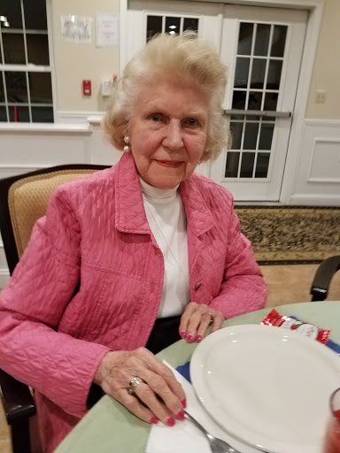 An elderly woman in a pink jacket enjoying a meal.