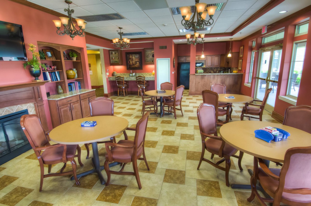 A cozy dining area with several round tables and upholstered chairs, illuminated by elegant chandeliers.