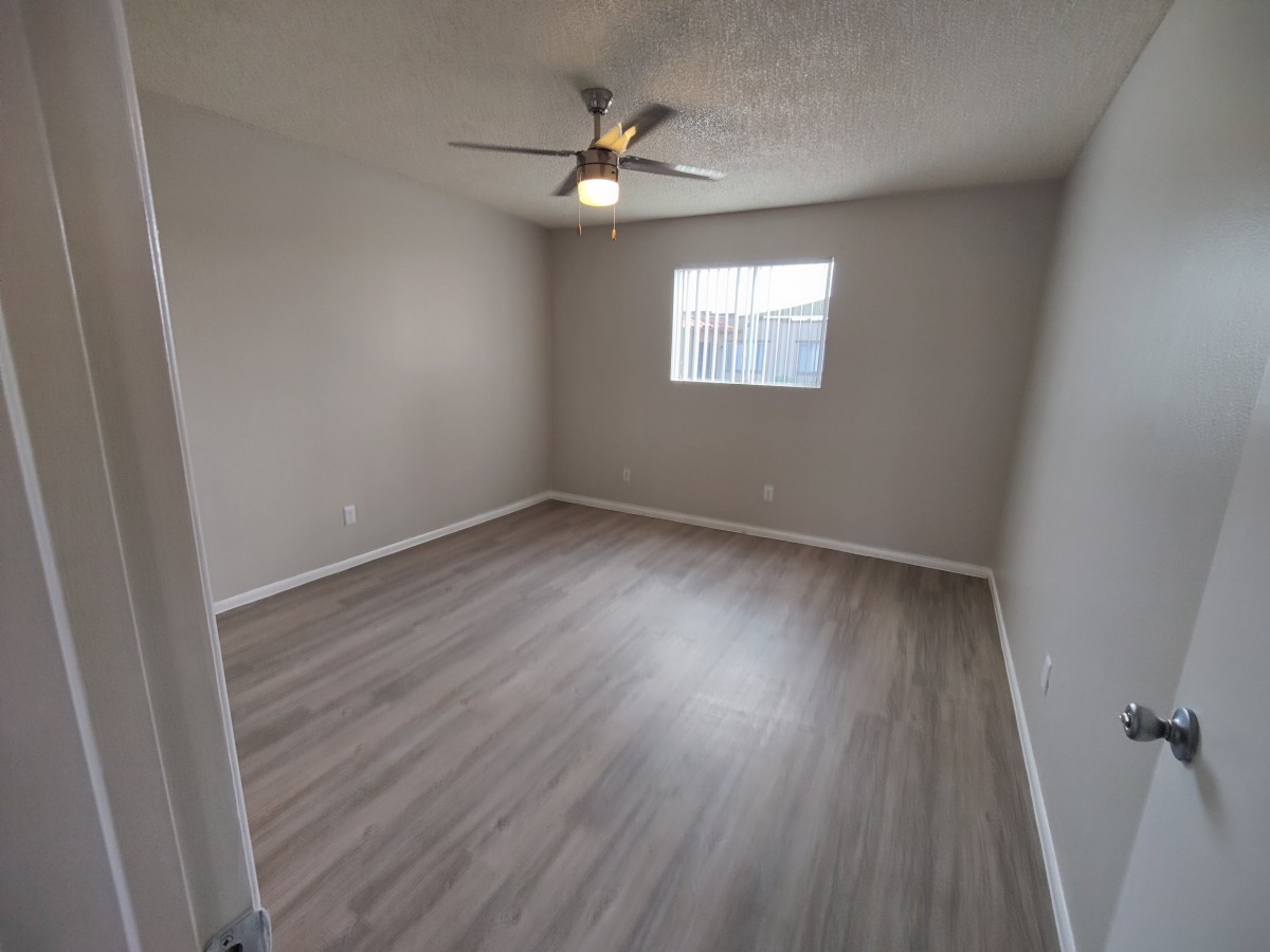 A spacious, empty room with wood flooring and a ceiling fan.
