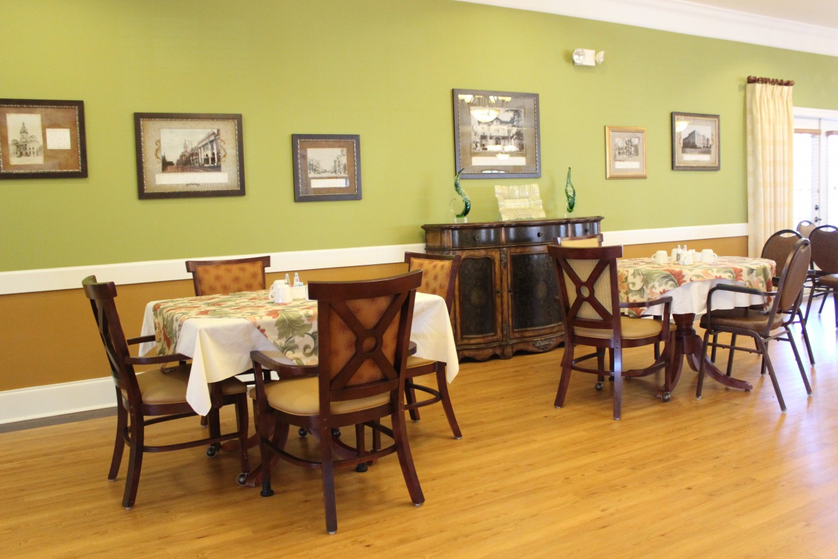 A cozy dining room with wooden furniture and green walls, featuring framed pictures and a sideboard.