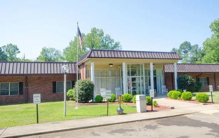 A small brick building with a flagpole and landscaped front area under a clear sky.