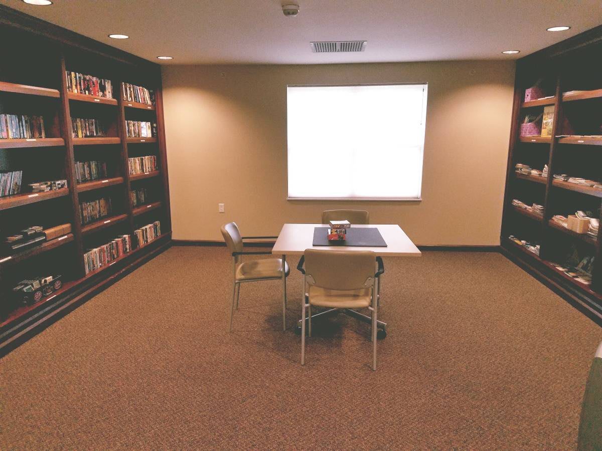 A quiet library reading room with bookshelves, a table, and chairs.