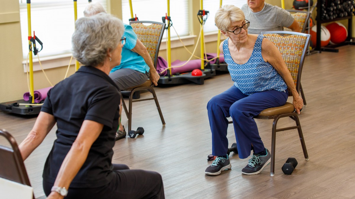 A group of elderly individuals participating in a seated fitness class indoors.