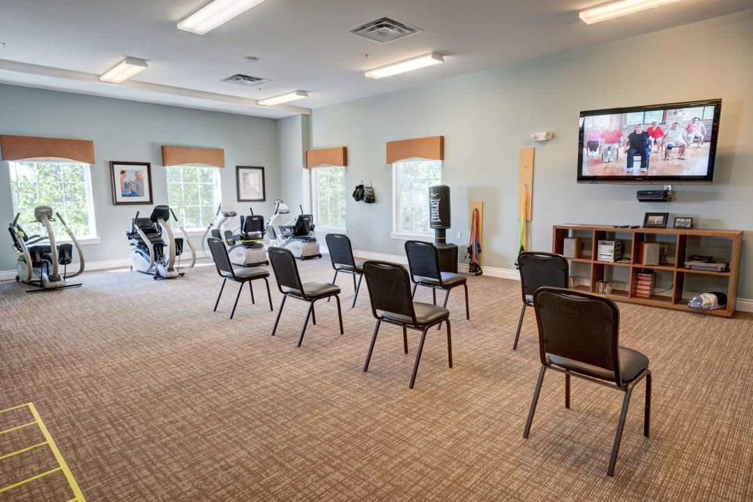 A fitness room with chairs arranged in rows and exercise equipment by the windows.