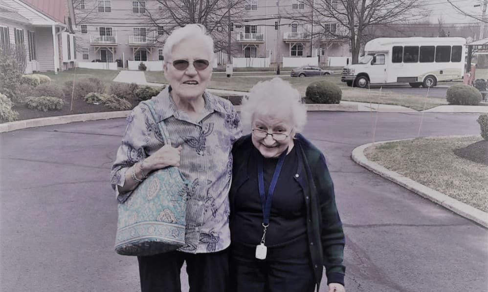 Two elderly women smiling and standing outside together.