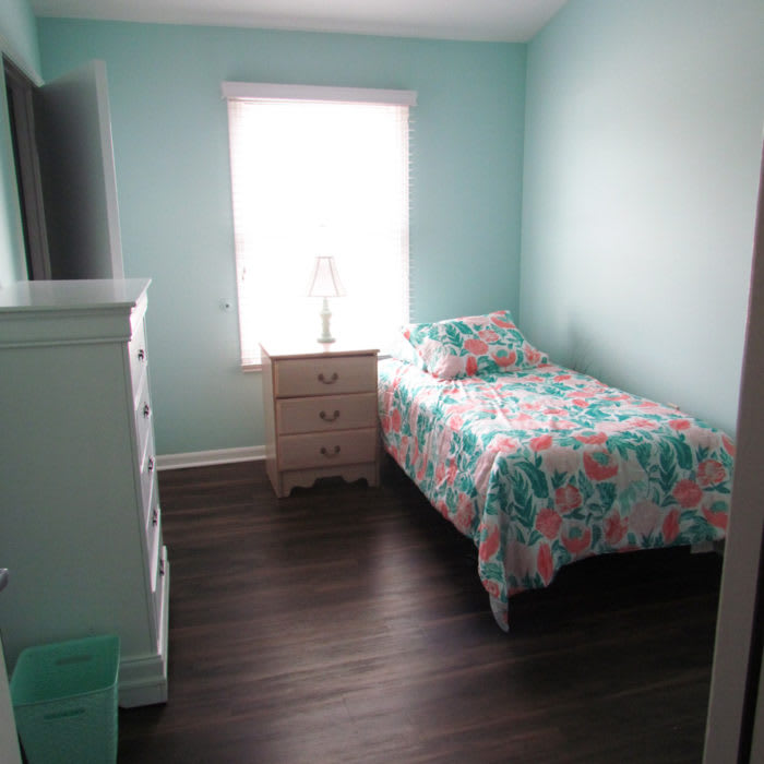 A minimalist bedroom with mint green walls and a single bed featuring a floral comforter.