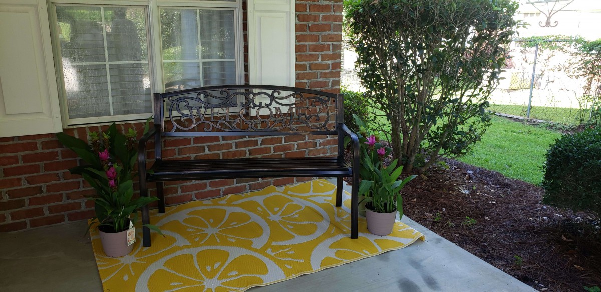 A cozy porch with a metal bench, lemon-patterned rug, and a potted plant.