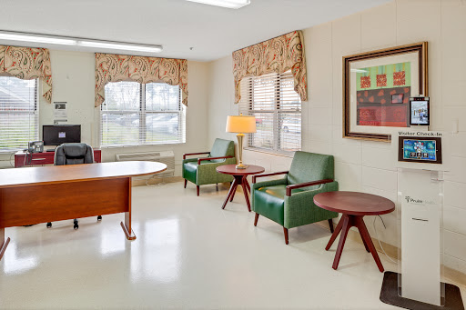 A cozy waiting area featuring comfortable green chairs, a wooden table, and decorative art on the wall.
