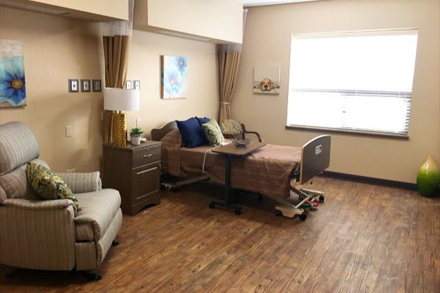 A well-furnished hospital room featuring a single bed, chair, and natural light from a window.