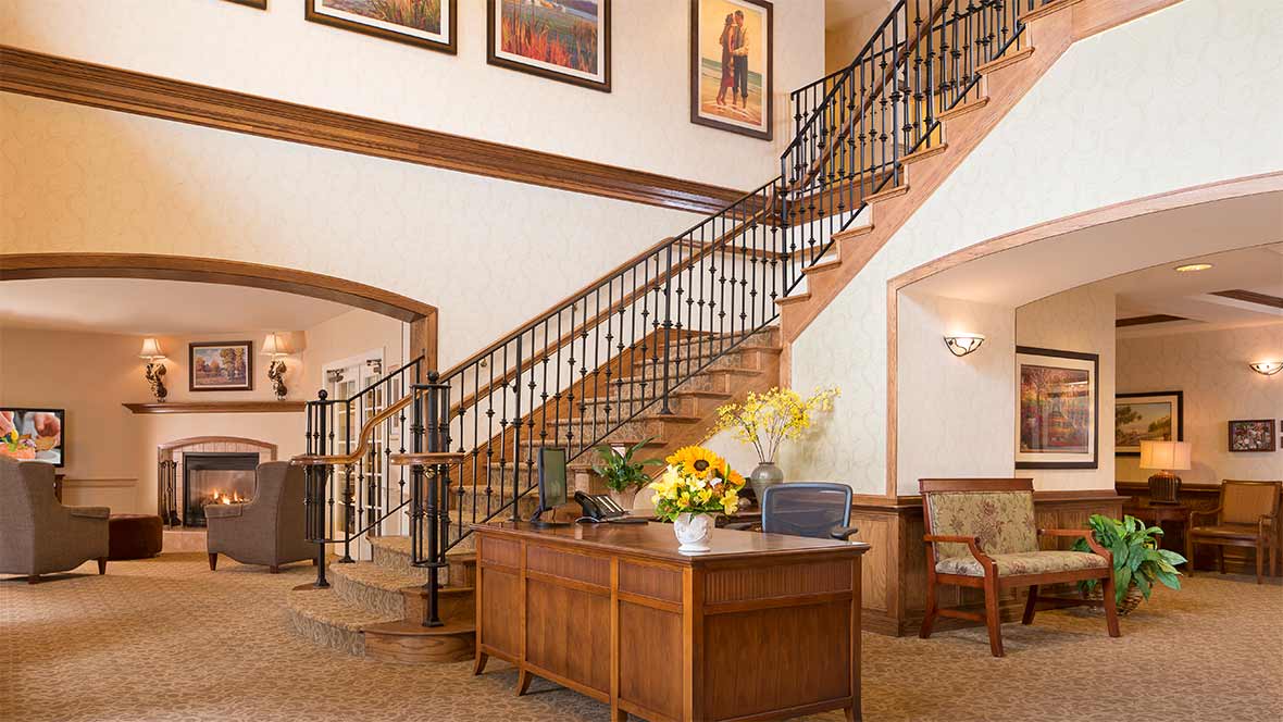 A welcoming reception area with a wooden desk, decorative flowers, and a staircase adorned with artwork.