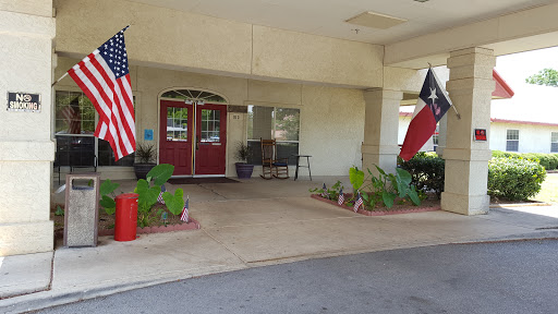 The welcoming entrance of a building adorned with American and Texas flags, surrounded by lush landscaping.