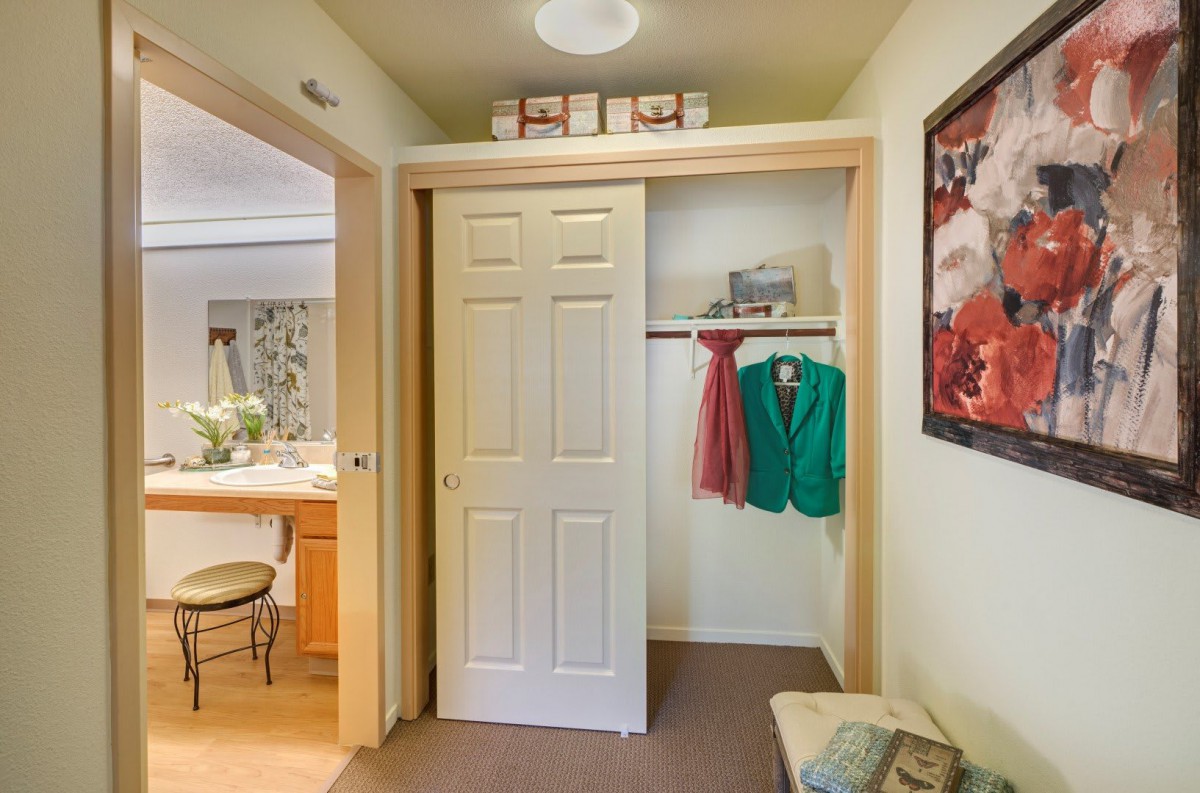 A cozy bedroom with an open closet showing colorful clothing and a sliding door.