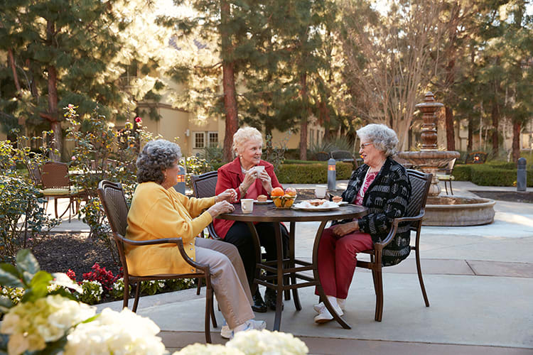 Three elderly women enjoying a conversation outdoors on a patio.