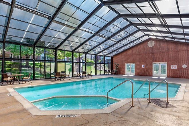 A spacious indoor swimming pool with a glass ceiling, featuring a spa area for relaxation.