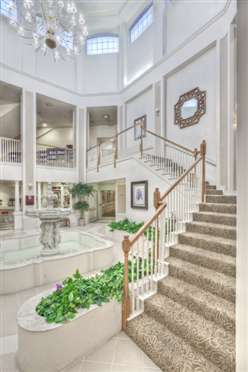 A bright, spacious interior featuring a grand staircase and a central fountain surrounded by lush greenery.