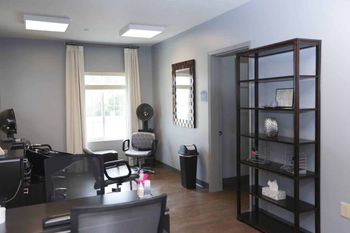 A tidy office meeting room with a large window, table, chairs, shelves, and bright lighting.