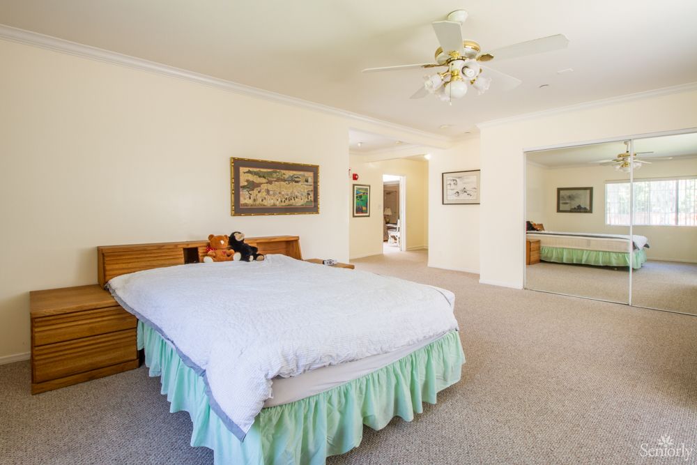 A spacious bedroom with a large bed, ceiling fan, and carpeted floor.
