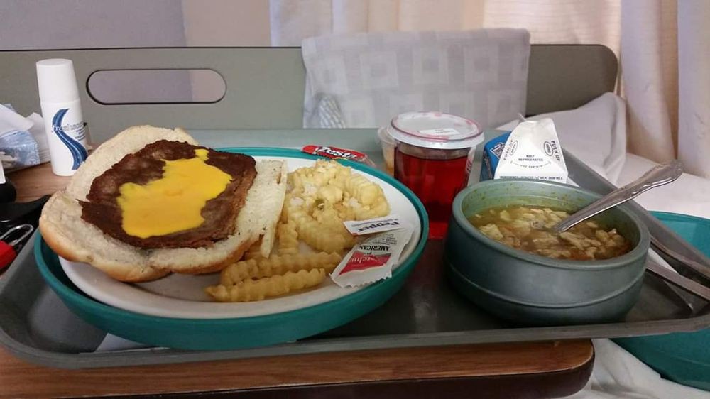 A hospital meal tray with a cheeseburger, fries, soup, and a drink.