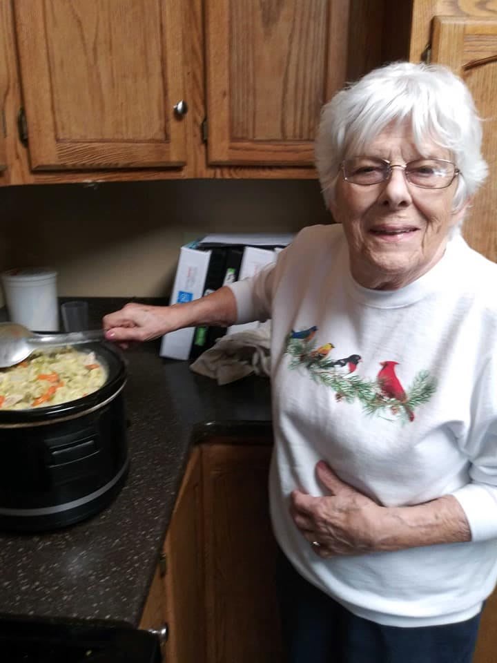 Elderly woman cooking in the kitchen, smiling at the camera.