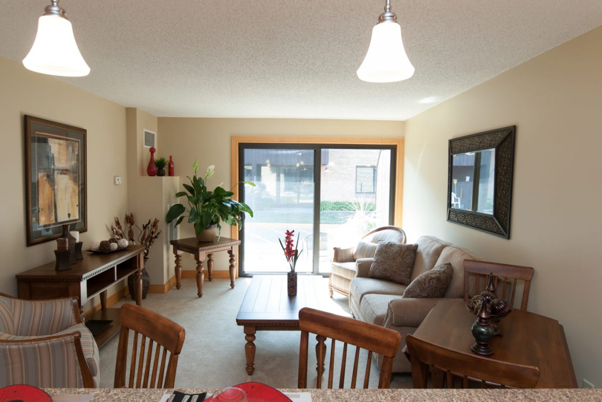 A cozy living room with a seating area, coffee table, dining chairs, and a large window providing natural light.