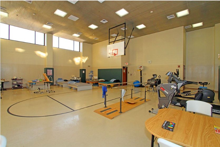 An indoor gym with a basketball hoop and various exercise equipment for rehabilitation and fitness activities.