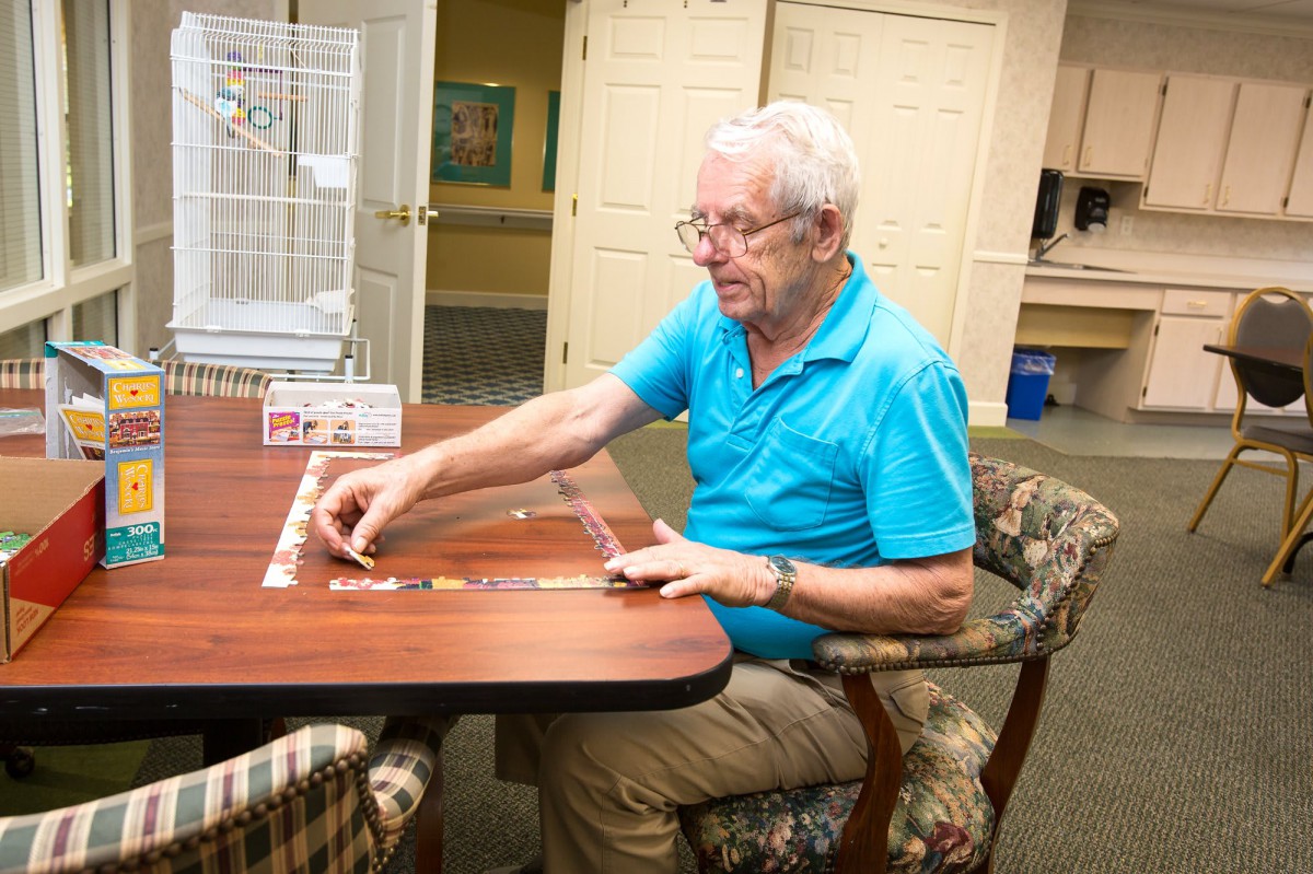 An elderly man engaged in assembling a puzzle at a table indoors.