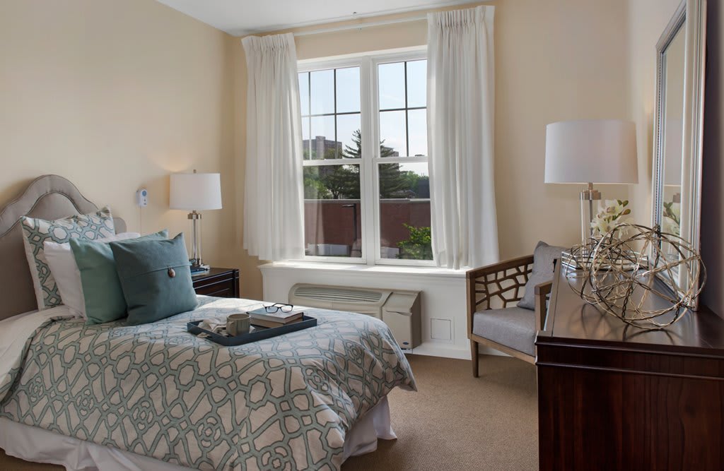 A cozy bedroom with a single bed, bedside lamps, and a large window with curtains.