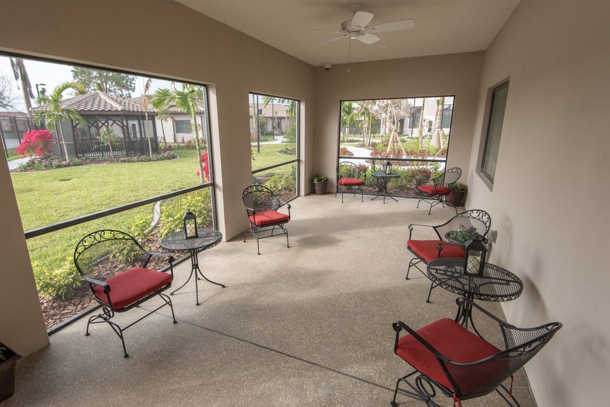 A screened patio with red-cushioned chairs and a garden view, offering a relaxing outdoor seating area.