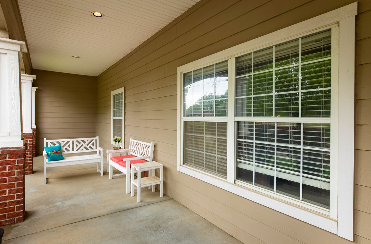 A cozy porch featuring two white benches with red cushions, next to windows with blinds.