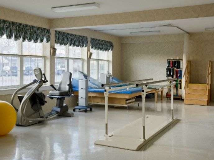 A physical therapy room equipped with parallel bars, stationary bikes, and therapy beds for rehabilitation purposes.