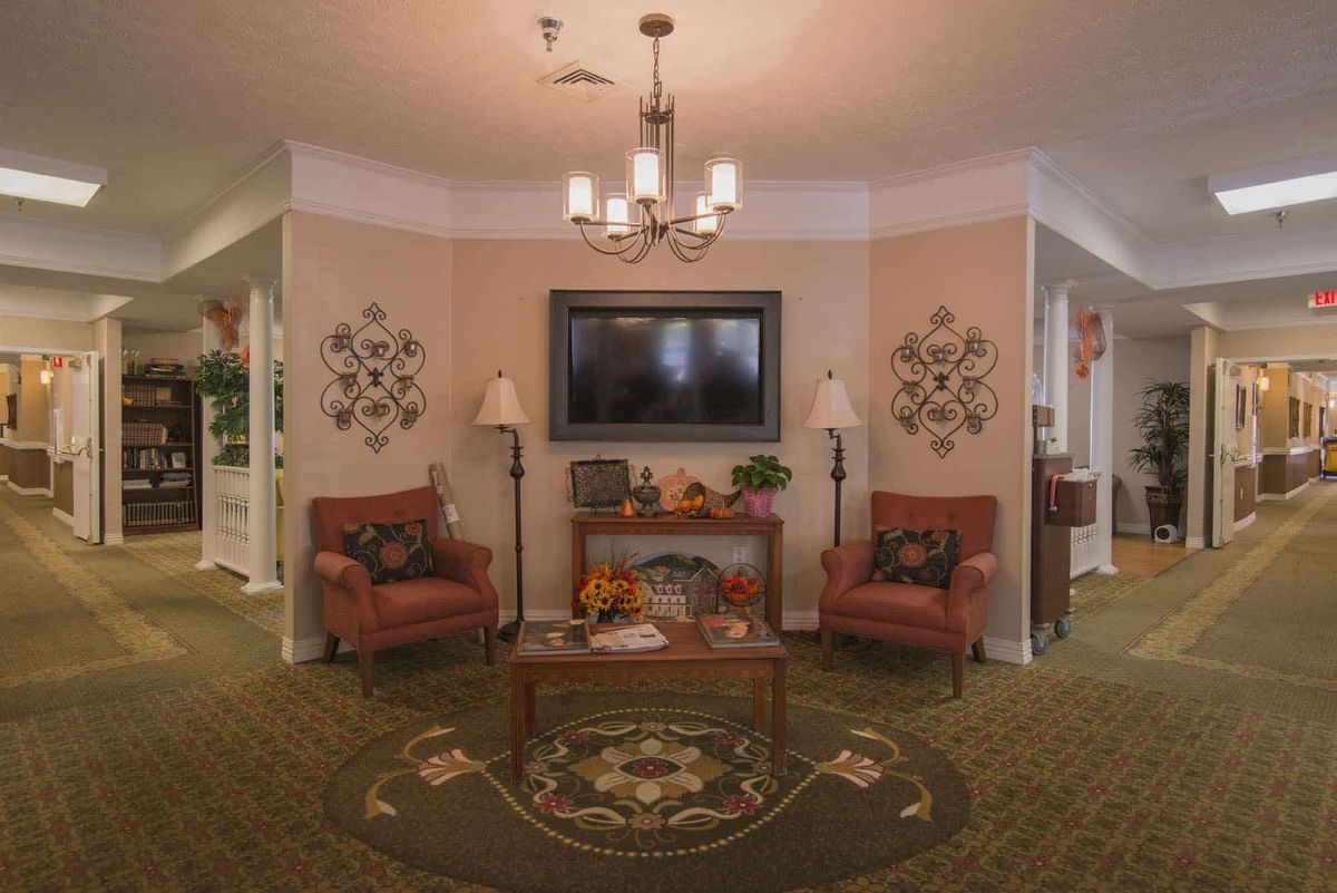 A cozy living room with traditional decor, featuring a chandelier, two armchairs, and wall art.