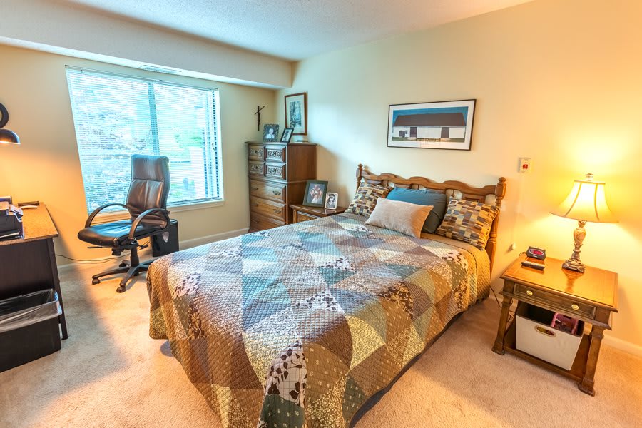 A cozy bedroom with a neatly made bed, chair, and desk near a large window.