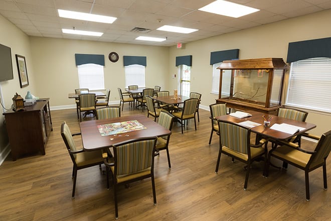 A cozy dining room with multiple tables and chairs, well-lit by overhead lights and natural light from the windows.