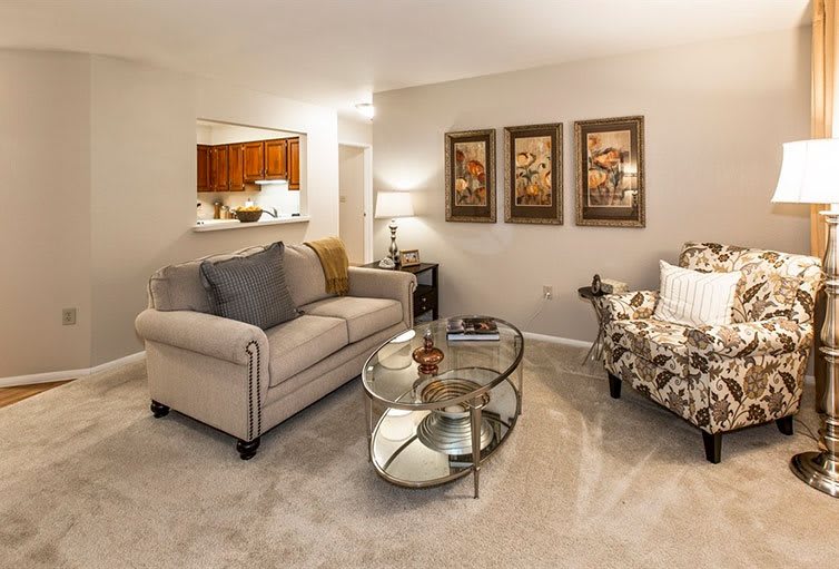A cozy living room with a sofa, armchair, and glass coffee table, accented by wall art and warm lighting.