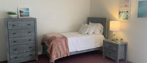 A minimalist bedroom featuring a single bed with white linens and decorative pillows.