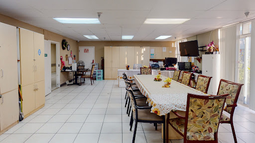 A spacious dining area featuring a long table set for meals, surrounded by comfortable chairs in a well-lit space.