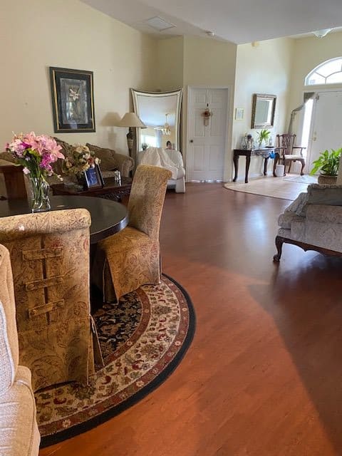 A cozy living room with a dining area, featuring elegant chairs around a round table, soft lighting, and decorative plants.