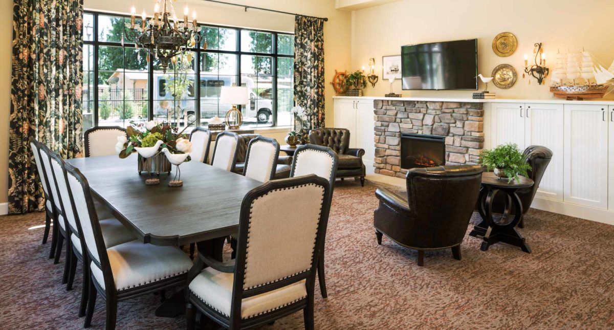 A cozy living and dining area featuring a fireplace, a large table with upholstered chairs, and a chandelier.