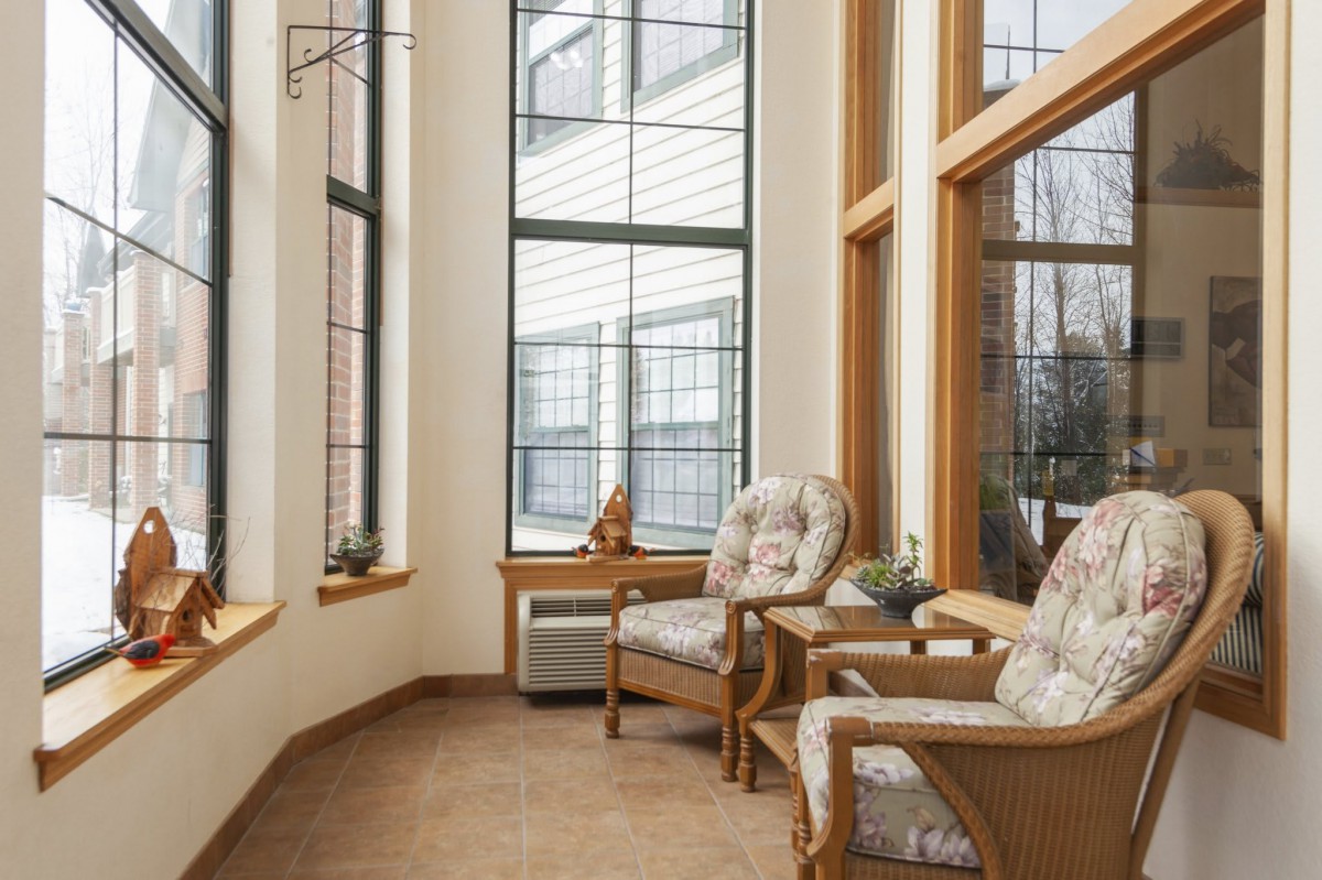 A cozy sunroom with large windows, featuring comfortable wicker chairs and natural lighting.