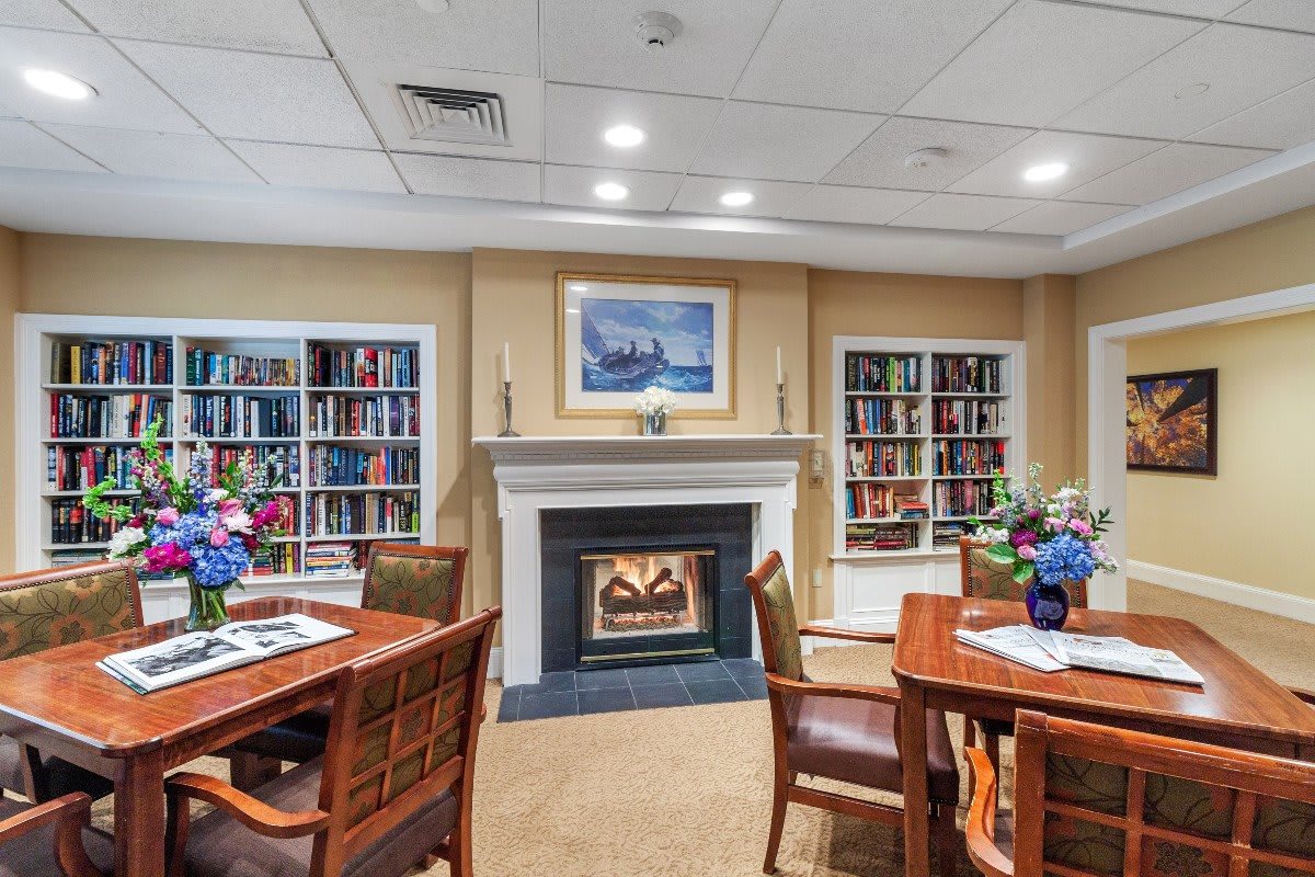 A cozy library setting with a fireplace, surrounded by bookshelves and seating areas.