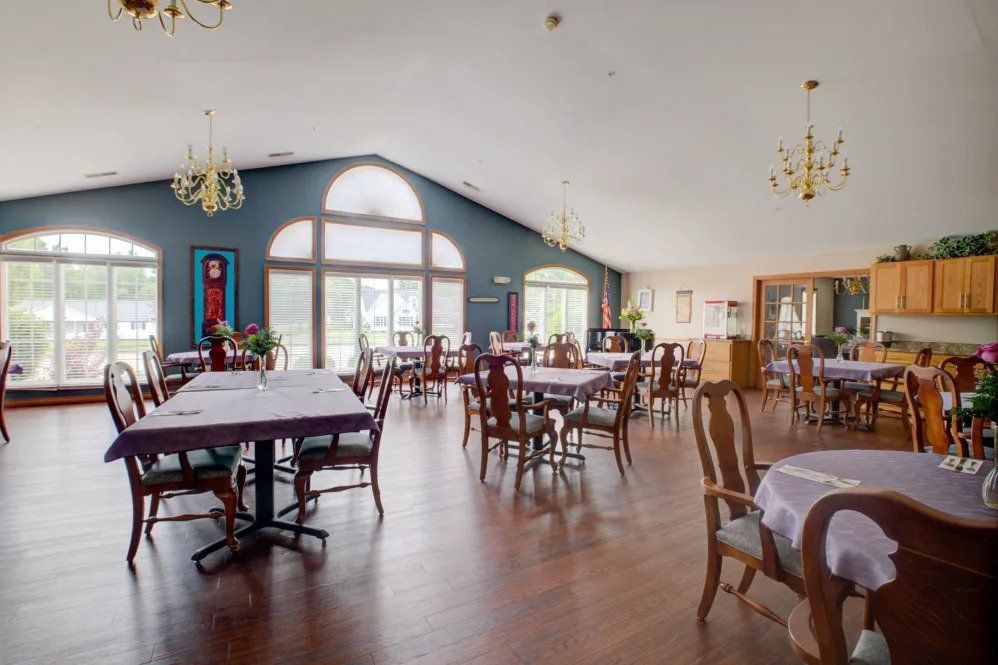 A spacious restaurant dining area with neatly arranged tables and chairs, featuring large windows and elegant chandeliers.